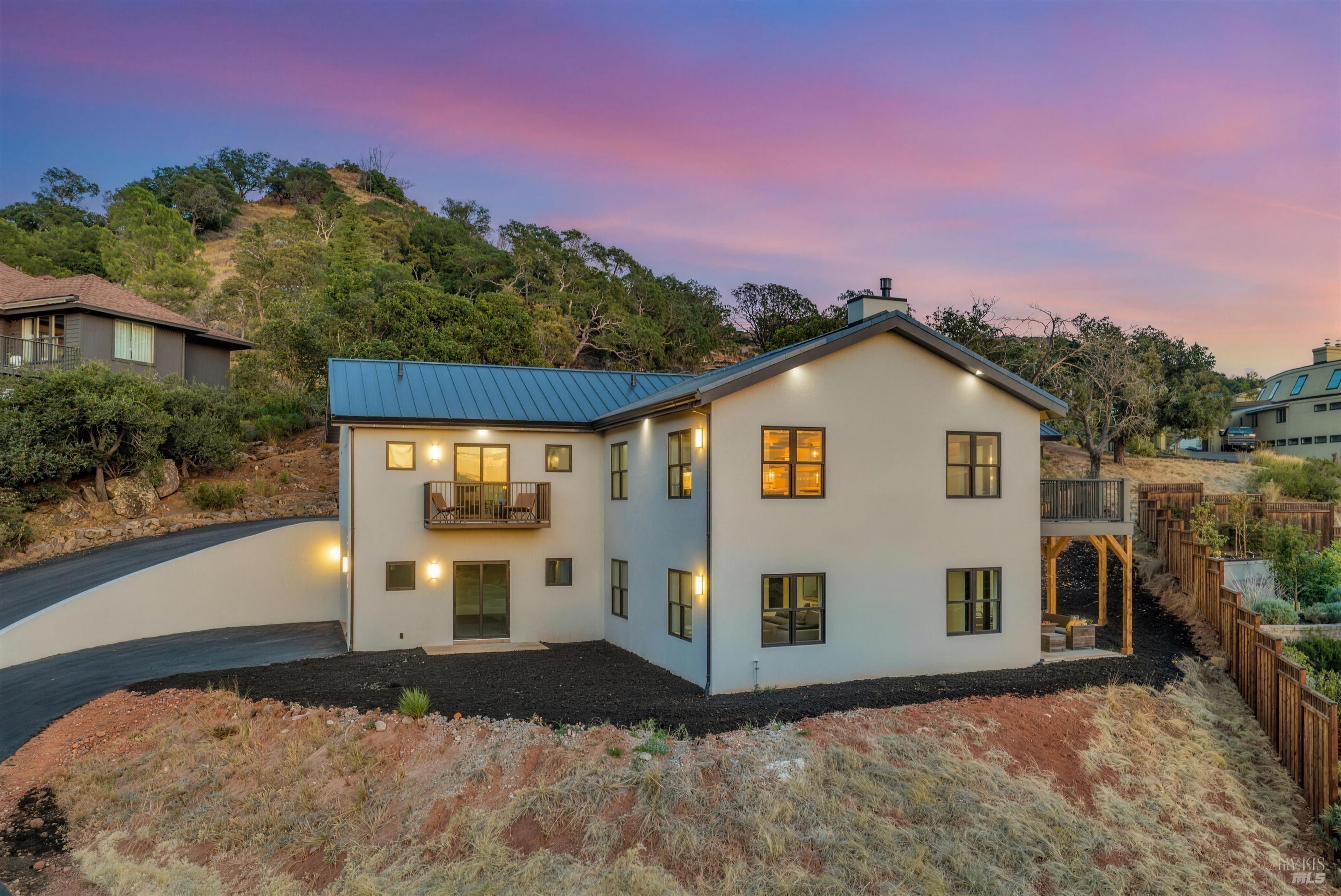 A new-construction Napa home lit from within at dusk on a wooded hillside